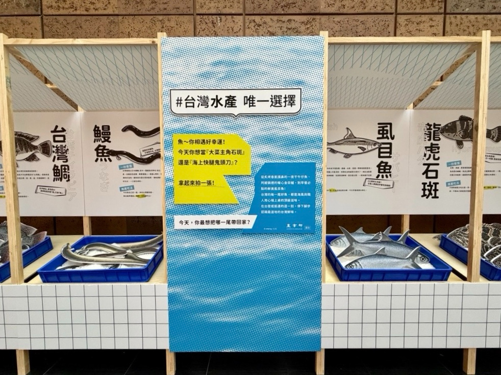 北車大廳貘魚廣場現場設置特色展區，以木質結構搭配藍白格紋，展示台灣代表性水產，並結合趣味問答立牌，讓旅客宛如置身海鮮市集。圖/農業部提供